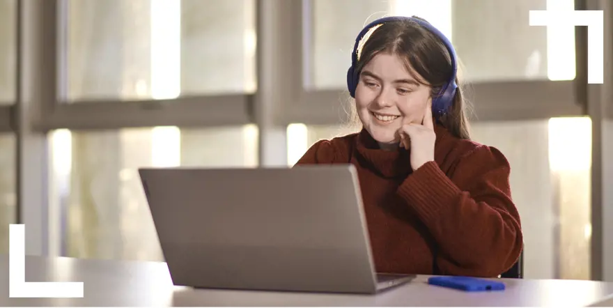 young woman wearing headphones smiling at computer screen